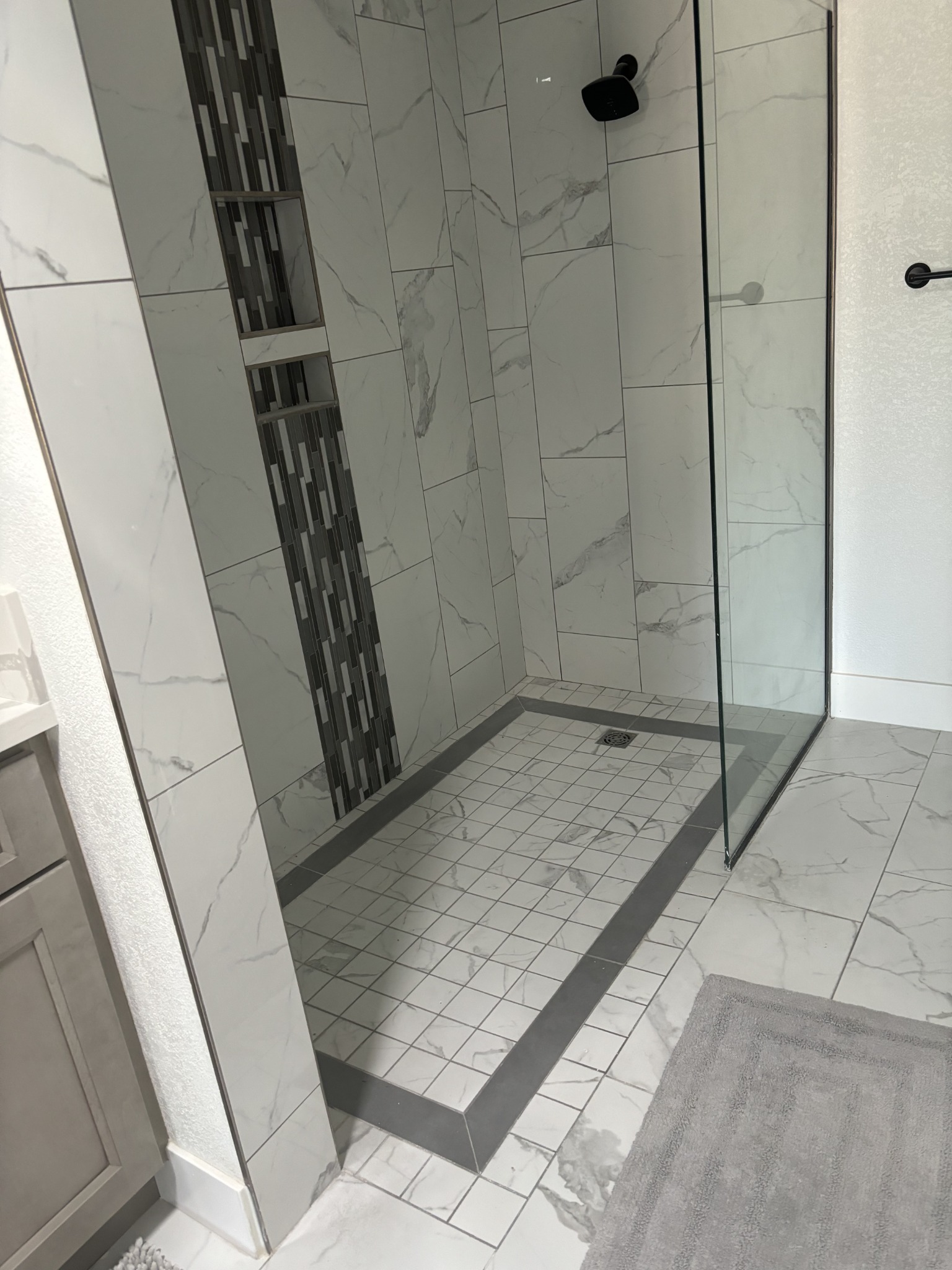 Completed MSWT walk-in shower with marble-look tile, glass enclosure, accent mosaic and built-in niches