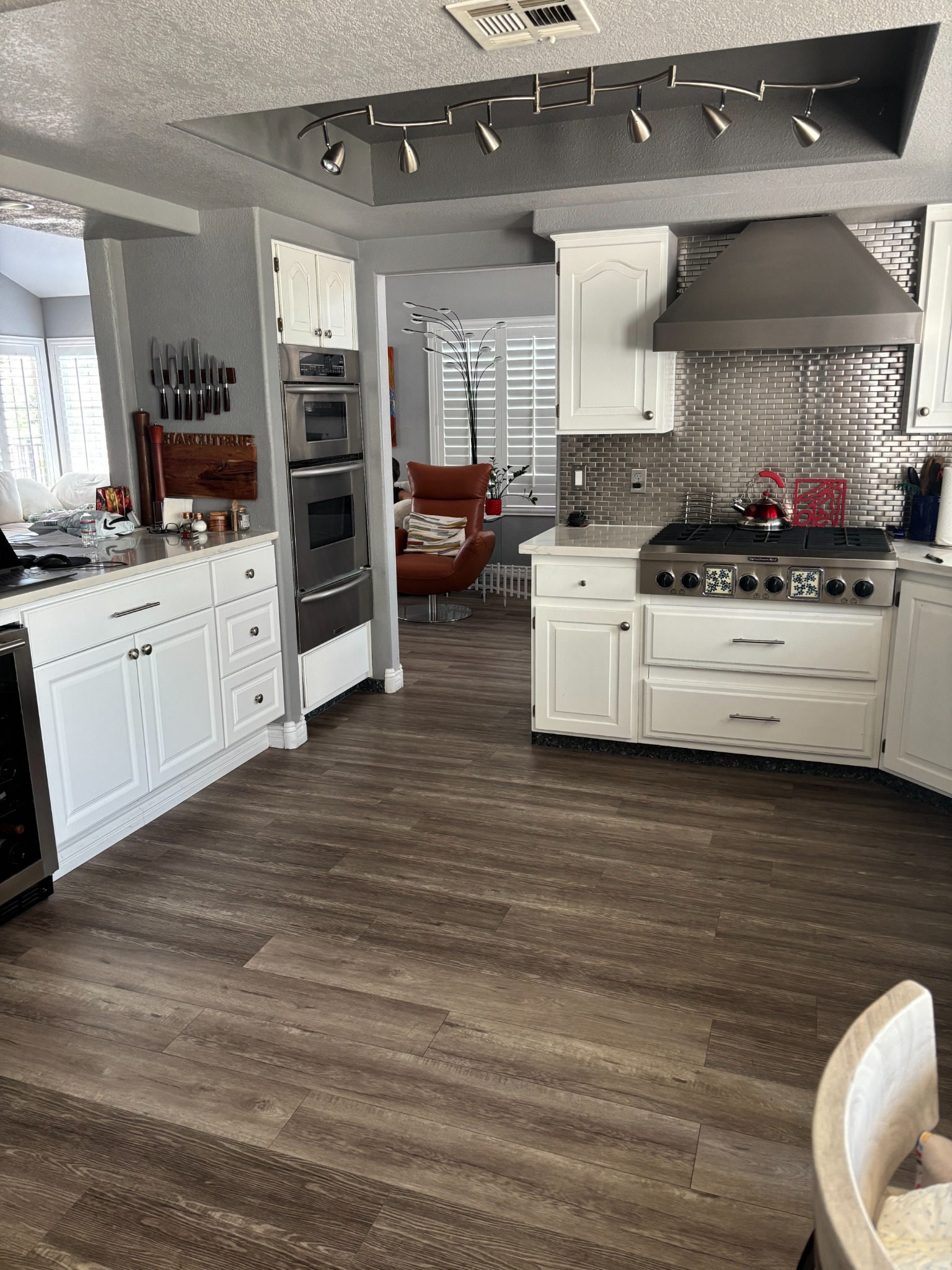 Completed MSWT kitchen remodel with white cabinetry, metallic tile backsplash, stainless steel range and wood-look flooring